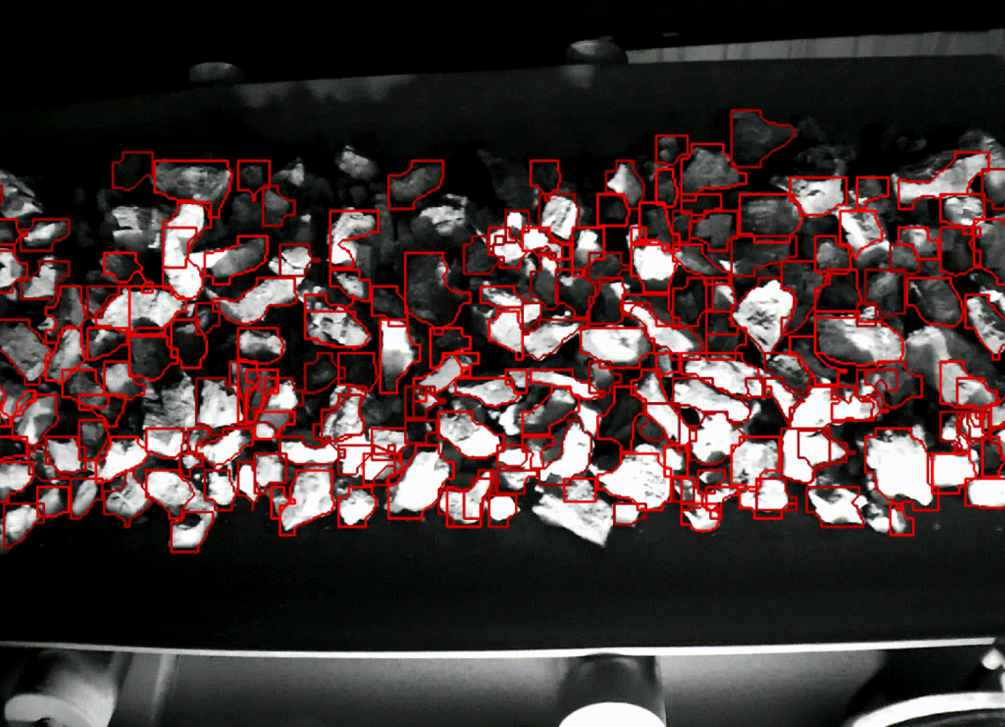 Black and white image of rocks on a conveyor belt, with red outlines highlighting individual pieces.
