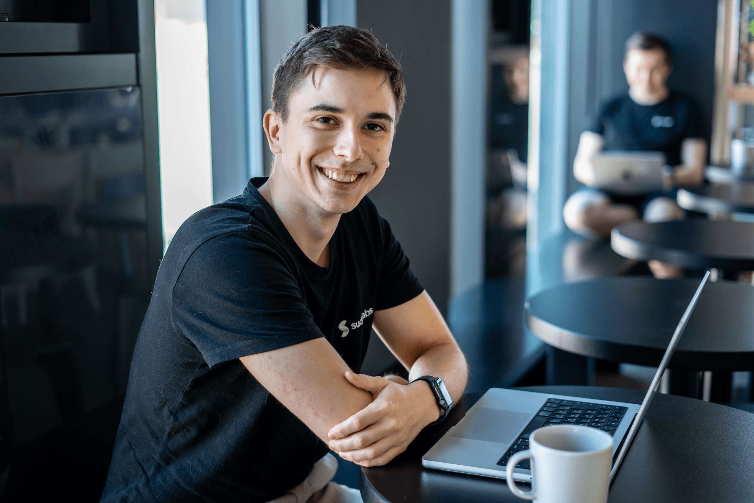 Erik Kandalík, seated at the office, with a warm smile, working on a computer and enjoying a cup of coffee